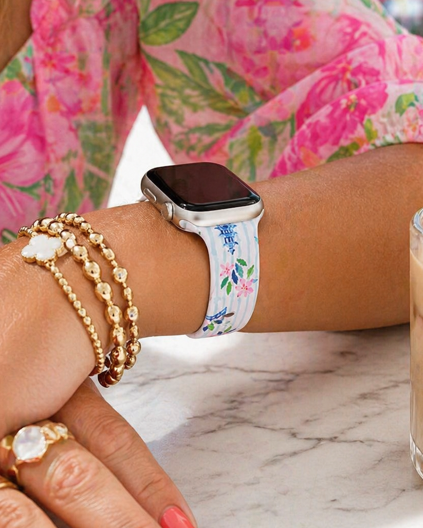 Person wearing a floral smartwatch and multiple bracelets with a drink in the background